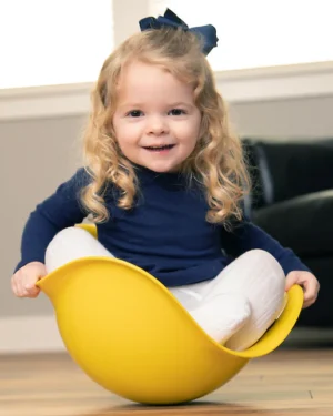 Bilibo en plastique coloré en forme de coque ouverte, utilisé par un enfant assis pour se balancer ou tourner, favorisant l’équilibre, la coordination motrice et l’imagination dès 2 ans