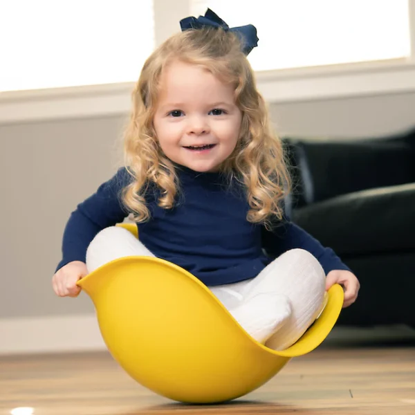 Bilibo en plastique coloré en forme de coque ouverte, utilisé par un enfant assis pour se balancer ou tourner, favorisant l’équilibre, la coordination motrice et l’imagination dès 2 ans