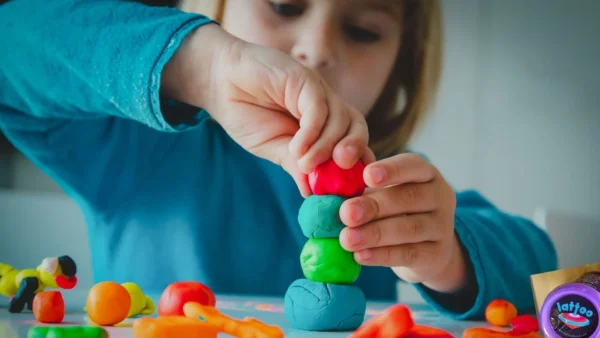 Enfant utilisant ses mains pour modeler de la pâte à modeler multicolore sur une surface claire, expérimentant différentes formes avec concentration et plaisir sensoriel .